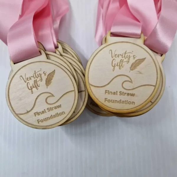 Four wooden running medals with pink ribbons.