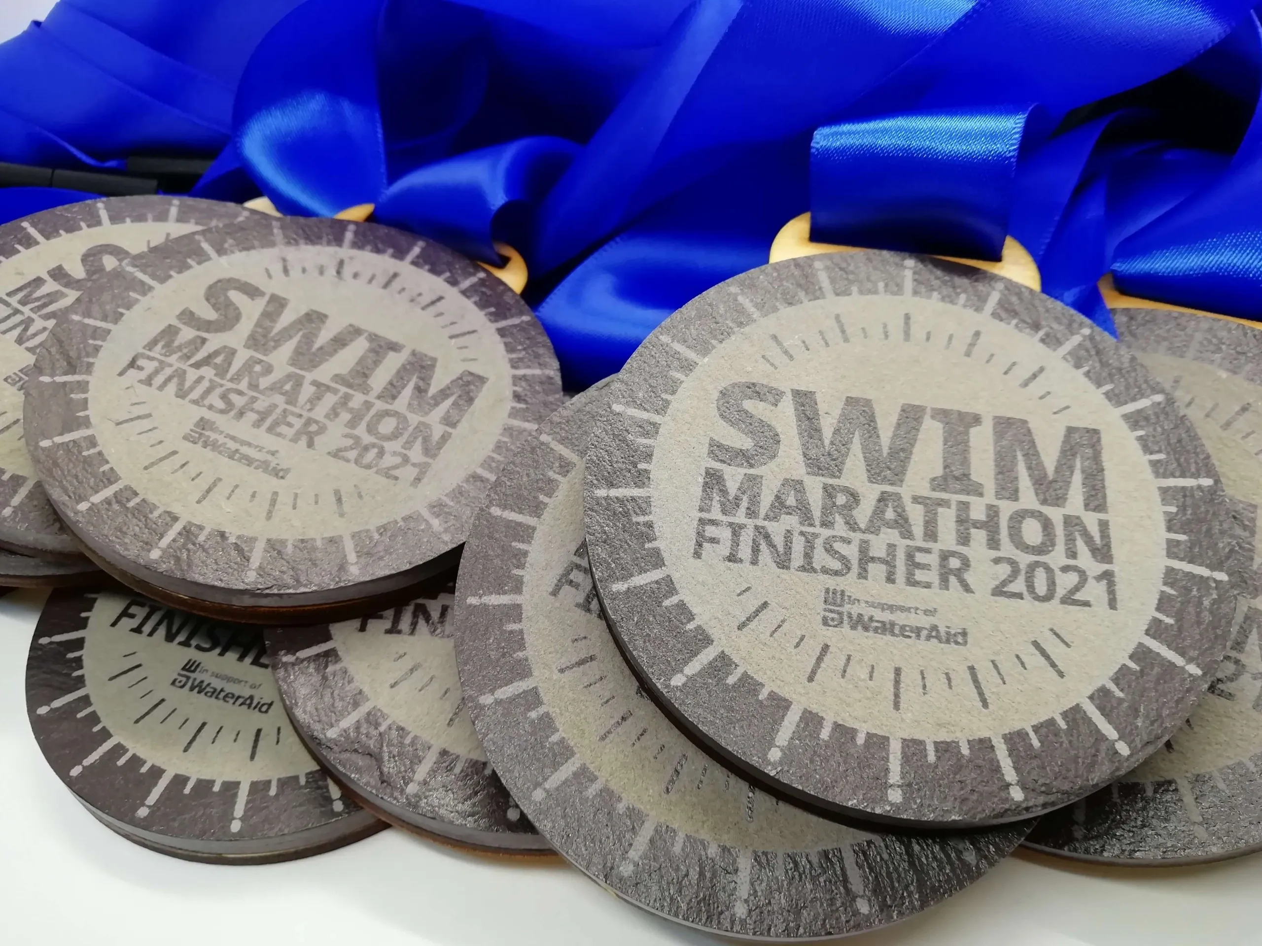 A group of Eco Friendly Slate Medals with the words swim marathon finisher 2021.