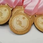 A group of wooden medals with pink ribbons.