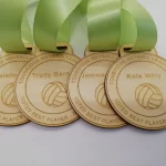 Four wooden volleyball medals with green ribbons.