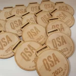 A group of wooden medals with the word qsa on them.