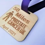 A wooden medal with the words 50 miles prostate cancer uk april 2021.