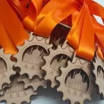 A collection of eco-friendly wooden medals adorned with vibrant orange ribbons.