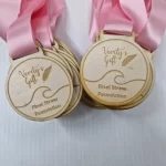 Four wooden medals with pink ribbons.