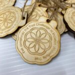 A pile of wooden medallions with engraved text reading "I've completed the Trail Challenge at Ingleton Waterfalls Trail" and an intricate circular design in the center, all attached to twine strings.