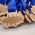 Wooden medals with blue ribbons for the "Geneva Cricket Cup 2024" are arranged in a pile.