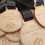 Wooden medals with black ribbons engraved with "PXO Wellbeing Challenge 2023" and a lotus symbol.