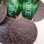 Close-up of several bronze medals with "LAKELAND BESPOKE 3000s" engraved, featuring a landscape design. Green ribbons attached.