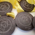 Several round medals with yellow ribbons, engraved with "Snowdonia Challenge 27th April 2024" and "Congratulations" along with mountain and pine tree designs.