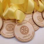 Wooden medals with yellow ribbons, inscribed with "District 1010," "FINALIST," and "Primary Schools Quiz 2024," featuring a rotary emblem.