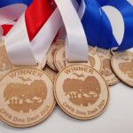 Wooden winner medals with red, white, and blue ribbons labeled "CPFR Dino Dash 2024" displayed on a flat surface.