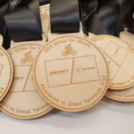 Close-up of wooden medals engraved with "600 Miles for Minds," logos, and "Aberdeen to Great Yarmouth 2024," featuring a cyclist icon and black ribbons.