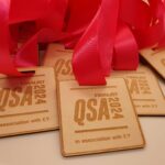 A pile of wooden medals with pink ribbons, labeled "FINALIST QSA 2024 in association with EY.