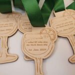 Three wooden medals shaped like cocktail glasses with green ribbons, engraved with "I walked 60 miles along the North Downs Way, 1st June 2024.