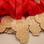 A pile of wooden medals with red ribbons, engraved with "Woodford Green Preparatory School" and a torch emblem.