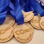 Pile of wooden medals with blue ribbons, engraved with "Cheeky Chimps Sports Day 2024" and cartoon characters.