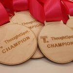 Close-up of several wooden medals engraved with "ThoughtSpot Champion," featuring pink ribbons.