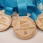 Wooden medals with turquoise ribbons from the Chipstead Sailing Club Mid-Summer Regatta 2024, featuring categories like 1st Junior Helm and 1st Mixed Boat.