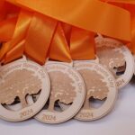 A collection of wooden medals with orange ribbons, engraved with "Mulberry Outdoor Sports Day 2024" and an image of a tree.