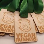 Wooden medals with green ribbons, engraved with a pig illustration and the text "Tower Hill Stables Animal Sanctuary Vegan Runners.