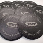 Several round slate coasters with "Thames Valley Triathletes" logo and text, including "Club Champion 2024" and various event titles like "OW Swim Open" and "Sprint.