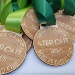 Wooden medals with green ribbons, engraved with "STEP OUT," "London to Brighton," "100km Challenge 2024.