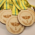 A pile of wooden medals with yellow and green ribbons, engraved with "16th Buccleuch Property Challenge" and the number "1".