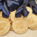 A pile of wooden medals with dark blue ribbons, engraved with "Waterbeach" and icons for swimming, biking, and running.