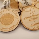 Wooden medals with engravings: "Latymer, North Kensington, Est. 2024, Dawn Til Dusk" on one side, "1 Mile Relay, 6:21 AM - 7:34 PM, 07.09.24" on the other.