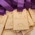 Wooden medals with purple ribbons, engraved with "Gullane Beach Triathlon" and images of athletes and a sun icon.