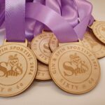 Wooden medals with purple ribbons, engraved with "Gin & Spin Sportive 2024" and "Sixty @ 60" along with the Spin logo featuring a bicycle wheel and cocktail glass design.