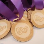 Wooden medals with purple ribbons display the word "Bibs" and the phrase "Saving Tiny Lives.