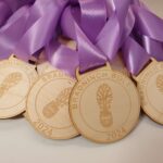 A group of wooden medals with purple ribbons, each engraved with BRADNINCH BOLT 2024 and a shoe design.