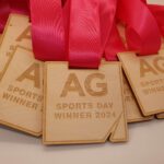 A pile of wooden medals with red ribbons, engraved with AG SPORTS DAY WINNER 2024.