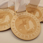 Four wooden medals with white ribbons display a design featuring bunny silhouettes, the text BunRun 2024, and The Bunny Jackpot Foundation printed around the edges.