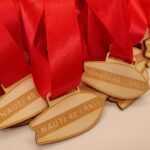 A pile of wooden medals with red ribbons, shaped like a lifeboat, engraved with NAUTI 40 RNLI.