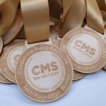 Close-up of wooden medals with gold ribbons, featuring the text CMS law.tax.future and Corporate Away Day 2024 Tech Hackathon Winner engraved on them. Medals are stacked with some overlapping.