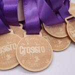 A collection of wooden medals with purple ribbons is laid out. The medals have the words Crossro and Barbell etched into them, along with a small barbell illustration.