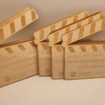 A set of wooden awards shaped like clapperboards with engraved text, including BA (Hons) AFs&S Film Awards, BEST PRODUCTION DESIGN, WRITING (ORIGINAL SCREENPLAY), and University of East London Student Life.