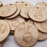 A pile of wooden tags engraved with Thank You for choosing Lily Pad Weddings & Events. The tags are oval-shaped with a hole at the top for hanging.