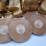 Wooden medals with Heaton Half 2024 engraved on them are laid out. Each medal has a golden ribbon attached.