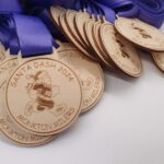 A pile of wooden medals with blue ribbons, engraved with Santa Dash 2024 and Monkton Millers. The medals feature a cartoon image of Santa Claus running.