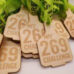 A pile of wooden medals with 10s 269 Challenge engraved on them, attached to bright green ribbons that read GREENMILES FITNESS.