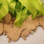 Close-up of several wooden leaf-shaped medals with Tammy Lake 8 km 2024 engraved on them. Each medal has a green ribbon attached, and theyre layered over each other.