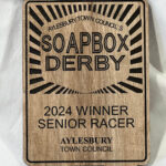 Wooden plaque awarded to the 2024 winner of the Soapbox Derby Senior Racer, presented by Aylesbury Town Council. The design includes bold text and decorative rays at the top.