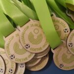 A pile of medals from the Goethe-Instituts Fussballcup event, dated 28.06.2024. The medals have neon green ribbons and feature a soccer ball graphic.