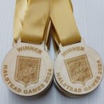 A set of gold medals with yellow ribbons, each engraved with WINNER HALSTEAD GAMES 2024 and the logo H.C.P.S.