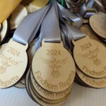 A pile of wooden medals with gray ribbons, engraved with 2024 Findhorn Regatta and a bird emblem.