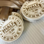 A close-up of several medals with brown ribbons, inscribed with Kenilworth Half Marathon & 5K 2024 and the word Runners around the edge. The medals are displayed on a white ridged background.