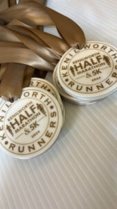 A close-up of several medals with brown ribbons, inscribed with Kenilworth Half Marathon & 5K 2024 and the word Runners around the edge. The medals are displayed on a white ridged background.